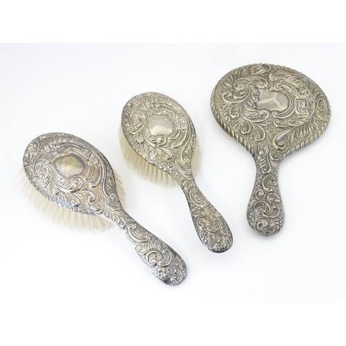 516 - A set of three silver dressing table items with embossed decoration comprising hand mirror and two b... 