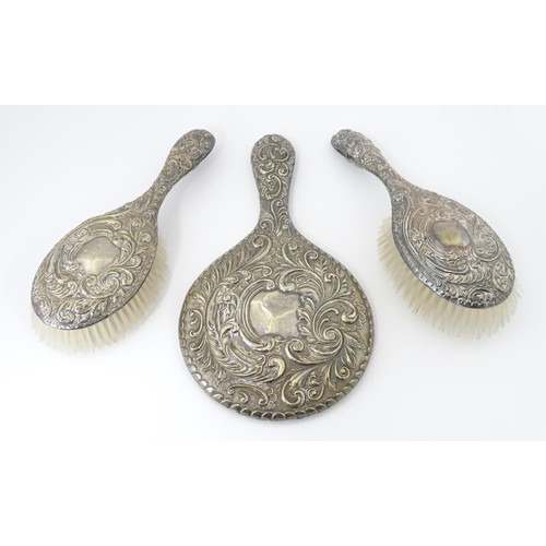 516 - A set of three silver dressing table items with embossed decoration comprising hand mirror and two b... 