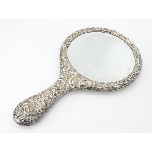 516 - A set of three silver dressing table items with embossed decoration comprising hand mirror and two b... 