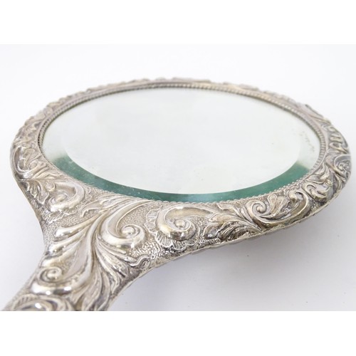 516 - A set of three silver dressing table items with embossed decoration comprising hand mirror and two b... 