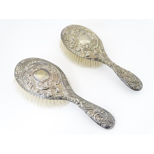 516 - A set of three silver dressing table items with embossed decoration comprising hand mirror and two b... 