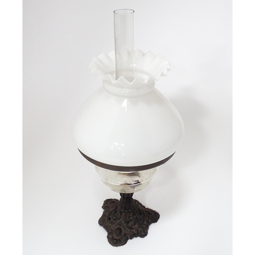 320 - An early 20thC table oil lamp with chimney and shade, the cast iron base supporting a clear glass re... 