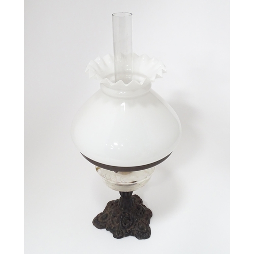 320 - An early 20thC table oil lamp with chimney and shade, the cast iron base supporting a clear glass re... 