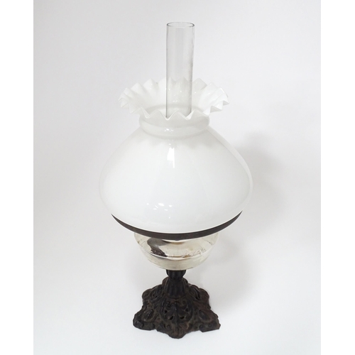 320 - An early 20thC table oil lamp with chimney and shade, the cast iron base supporting a clear glass re... 