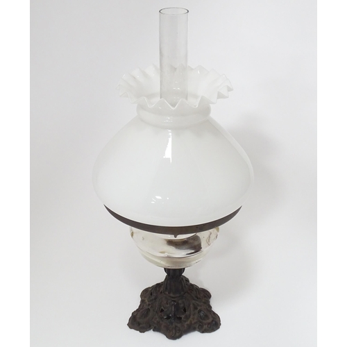 320 - An early 20thC table oil lamp with chimney and shade, the cast iron base supporting a clear glass re... 