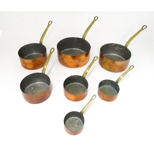 323 - Kitchenalia : a 20thC graduated set of seven copper saucepans, each with brass handle terminating in... 