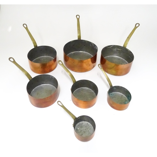 323 - Kitchenalia : a 20thC graduated set of seven copper saucepans, each with brass handle terminating in... 