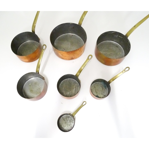 323 - Kitchenalia : a 20thC graduated set of seven copper saucepans, each with brass handle terminating in... 