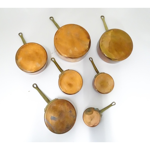 323 - Kitchenalia : a 20thC graduated set of seven copper saucepans, each with brass handle terminating in... 