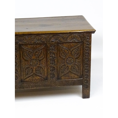 6 - An 18thC oak coffer with a hinged lid above four carved floral panels raise on stile feet. 59