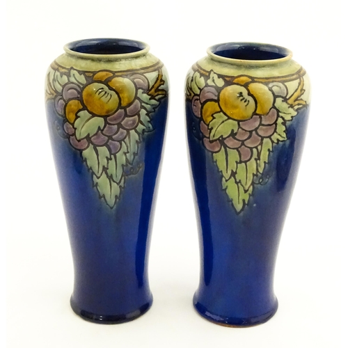 140 - A pair of Royal Doulton vases, the blue ground decorated with fruits and foliage. Marked under with ... 