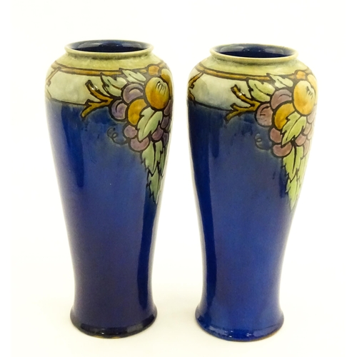 140 - A pair of Royal Doulton vases, the blue ground decorated with fruits and foliage. Marked under with ... 