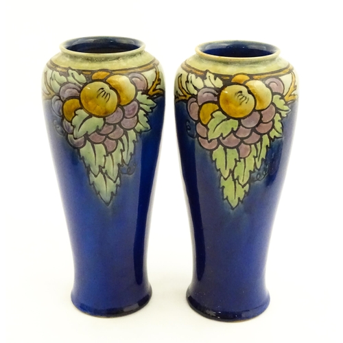 140 - A pair of Royal Doulton vases, the blue ground decorated with fruits and foliage. Marked under with ... 