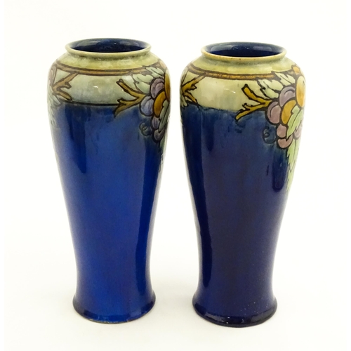 140 - A pair of Royal Doulton vases, the blue ground decorated with fruits and foliage. Marked under with ... 