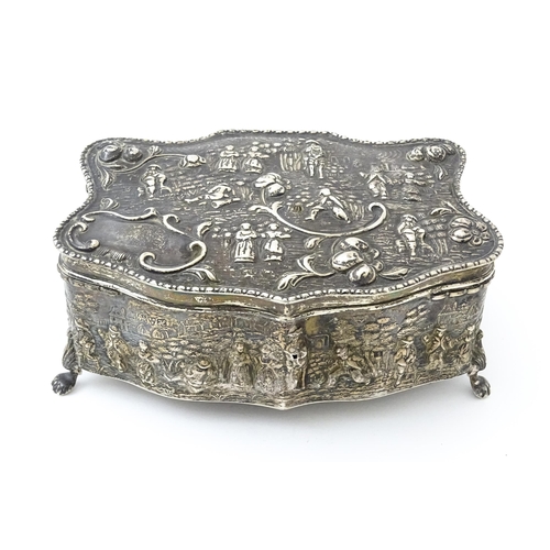 374 - An early 20thC silver jewellery box with embossed decoration depicting figures in landscape with hou... 