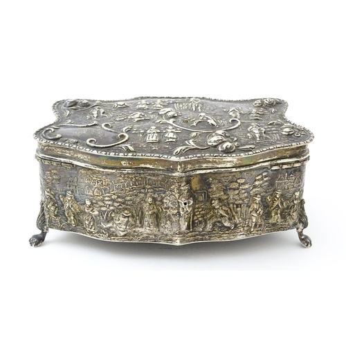 374 - An early 20thC silver jewellery box with embossed decoration depicting figures in landscape with hou... 