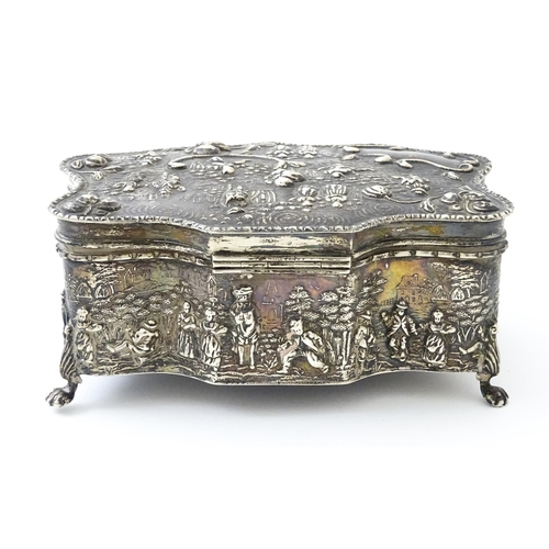 374 - An early 20thC silver jewellery box with embossed decoration depicting figures in landscape with hou... 