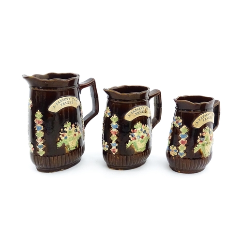 229 - A graduated set of three Victorian Measham bargeware jugs, each bearing a plaque titled A Present to... 