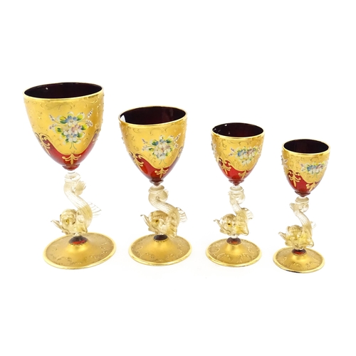 313 - A set of four graduated ruby glass and gilt goblets with dolphin formed stems. Largest approx. 7 1/2... 