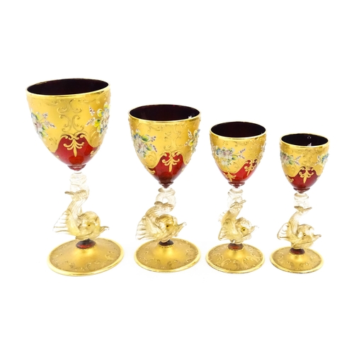 313 - A set of four graduated ruby glass and gilt goblets with dolphin formed stems. Largest approx. 7 1/2... 