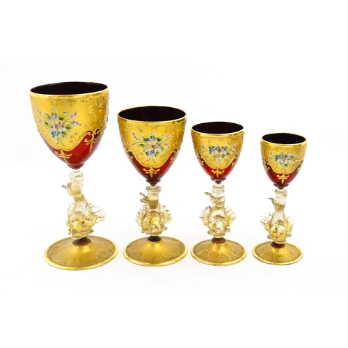 313 - A set of four graduated ruby glass and gilt goblets with dolphin formed stems. Largest approx. 7 1/2... 