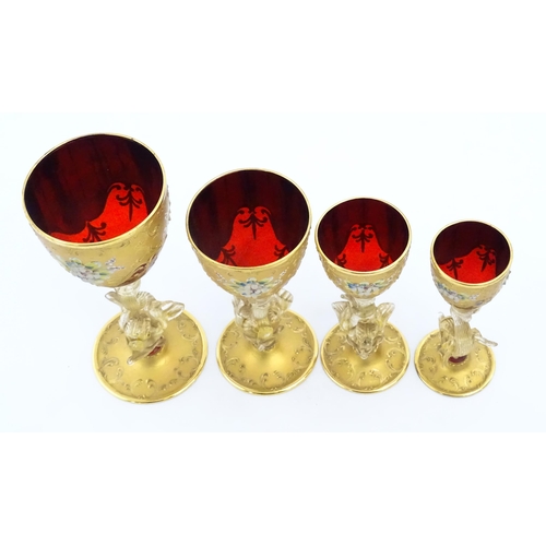 313 - A set of four graduated ruby glass and gilt goblets with dolphin formed stems. Largest approx. 7 1/2... 