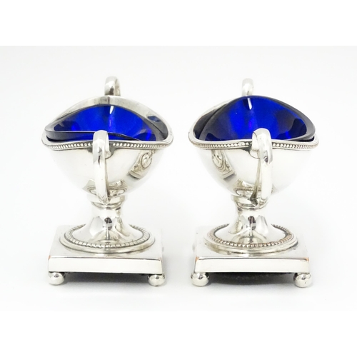 439 - A pair of silver plate twin handled pedestal salts of urn form, with blue glass liners. Together wit... 