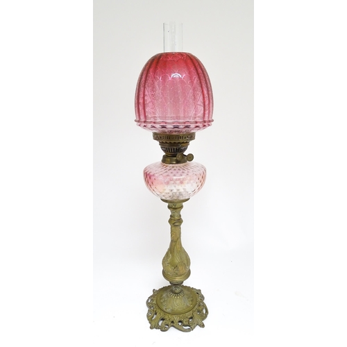 1701 - A Victorian brass oil lamp with floral and scroll detail, cranberry pink reservoir and shade. Approx... 