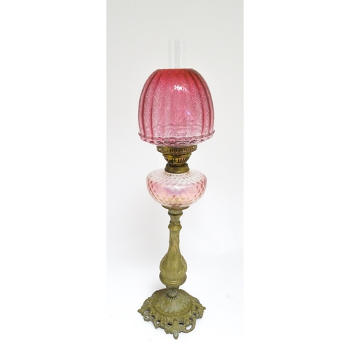 1701 - A Victorian brass oil lamp with floral and scroll detail, cranberry pink reservoir and shade. Approx... 