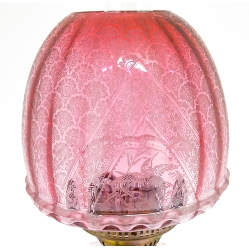 1701 - A Victorian brass oil lamp with floral and scroll detail, cranberry pink reservoir and shade. Approx... 