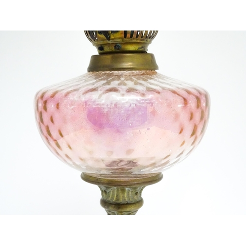 1701 - A Victorian brass oil lamp with floral and scroll detail, cranberry pink reservoir and shade. Approx... 