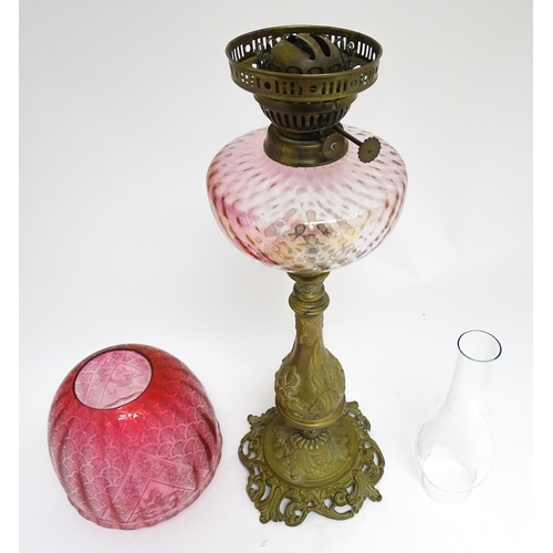 1701 - A Victorian brass oil lamp with floral and scroll detail, cranberry pink reservoir and shade. Approx... 