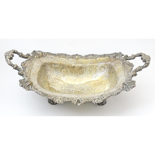 630 - A large George III silver twin handled dish with floral and C scroll decoration and raised on four l... 