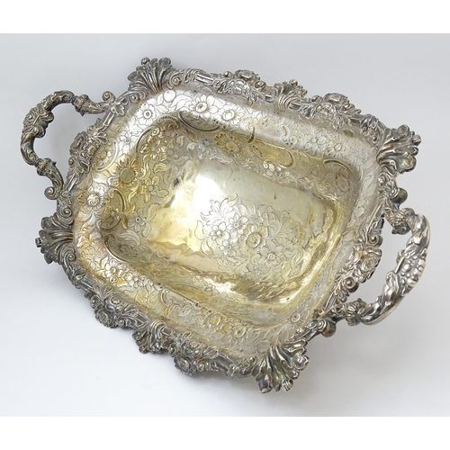 630 - A large George III silver twin handled dish with floral and C scroll decoration and raised on four l... 