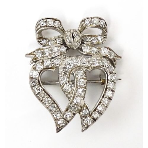 781 - A late 19thC / early 20thC brooch formed as two witches hearts surmounted by a bow set with diamonds... 