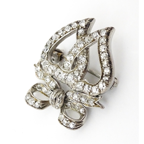 781 - A late 19thC / early 20thC brooch formed as two witches hearts surmounted by a bow set with diamonds... 