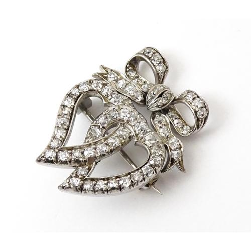 781 - A late 19thC / early 20thC brooch formed as two witches hearts surmounted by a bow set with diamonds... 