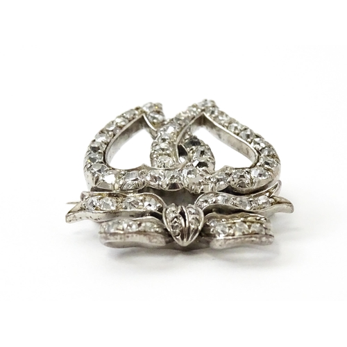 781 - A late 19thC / early 20thC brooch formed as two witches hearts surmounted by a bow set with diamonds... 