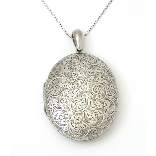 799 - A large white metal locket with engraved acanthus scroll decoration, on a white metal chain marked '... 