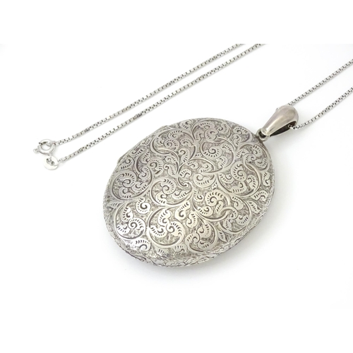 799 - A large white metal locket with engraved acanthus scroll decoration, on a white metal chain marked '... 