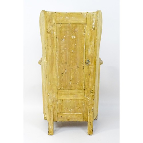 1839 - A pine lambing chair with a wingback above a planked seat and a cupboard to the base with H-bracket ... 