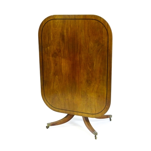 1900 - A late Georgian mahogany tilt top dining table with a ebonised stringing, a turned pedestal and rais... 