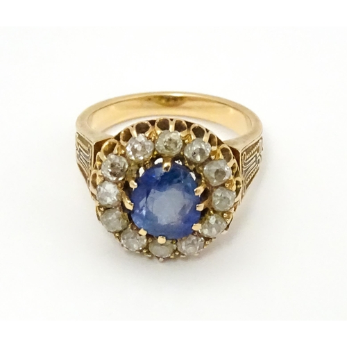 731 - A late 19thC / early 20thC gold ring set with central sapphire bordered by twelve diamonds flanked b... 