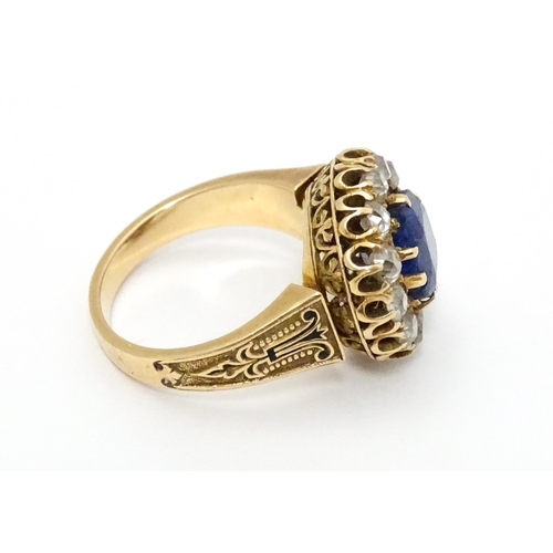 731 - A late 19thC / early 20thC gold ring set with central sapphire bordered by twelve diamonds flanked b... 