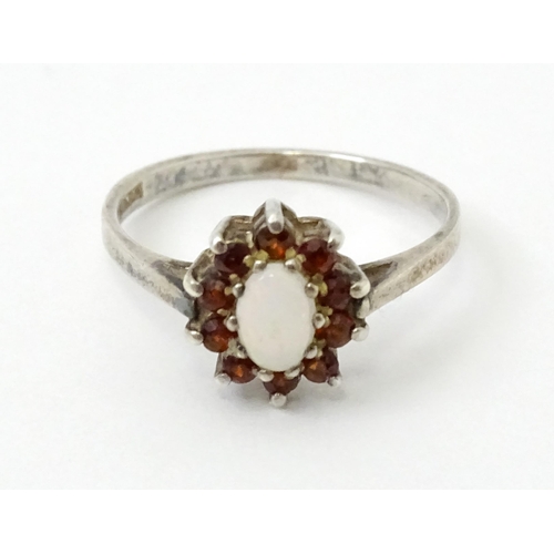 768 - A silver ring with set with central opal bordered by red stones. Ring size approx. P