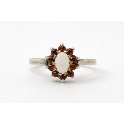 768 - A silver ring with set with central opal bordered by red stones. Ring size approx. P