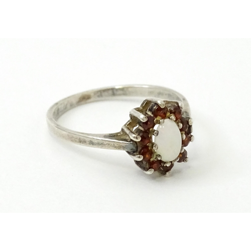 768 - A silver ring with set with central opal bordered by red stones. Ring size approx. P