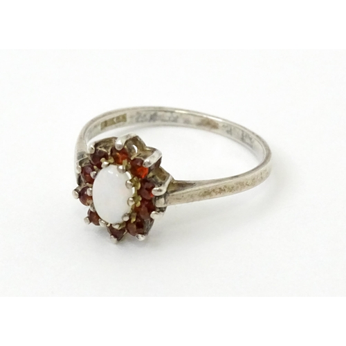 768 - A silver ring with set with central opal bordered by red stones. Ring size approx. P