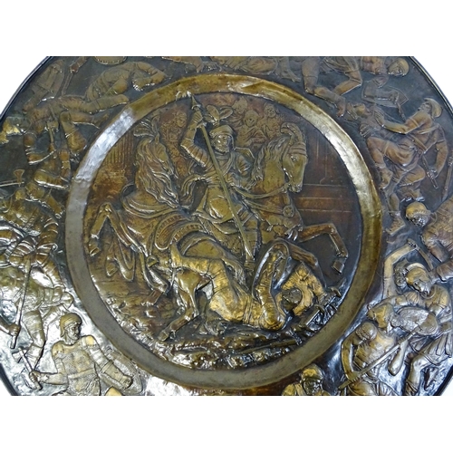 1507 - A large 20thC brass charger with relief decoration depicting Roman soldiers in battle, possibly depi... 