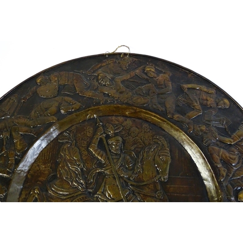 1507 - A large 20thC brass charger with relief decoration depicting Roman soldiers in battle, possibly depi... 